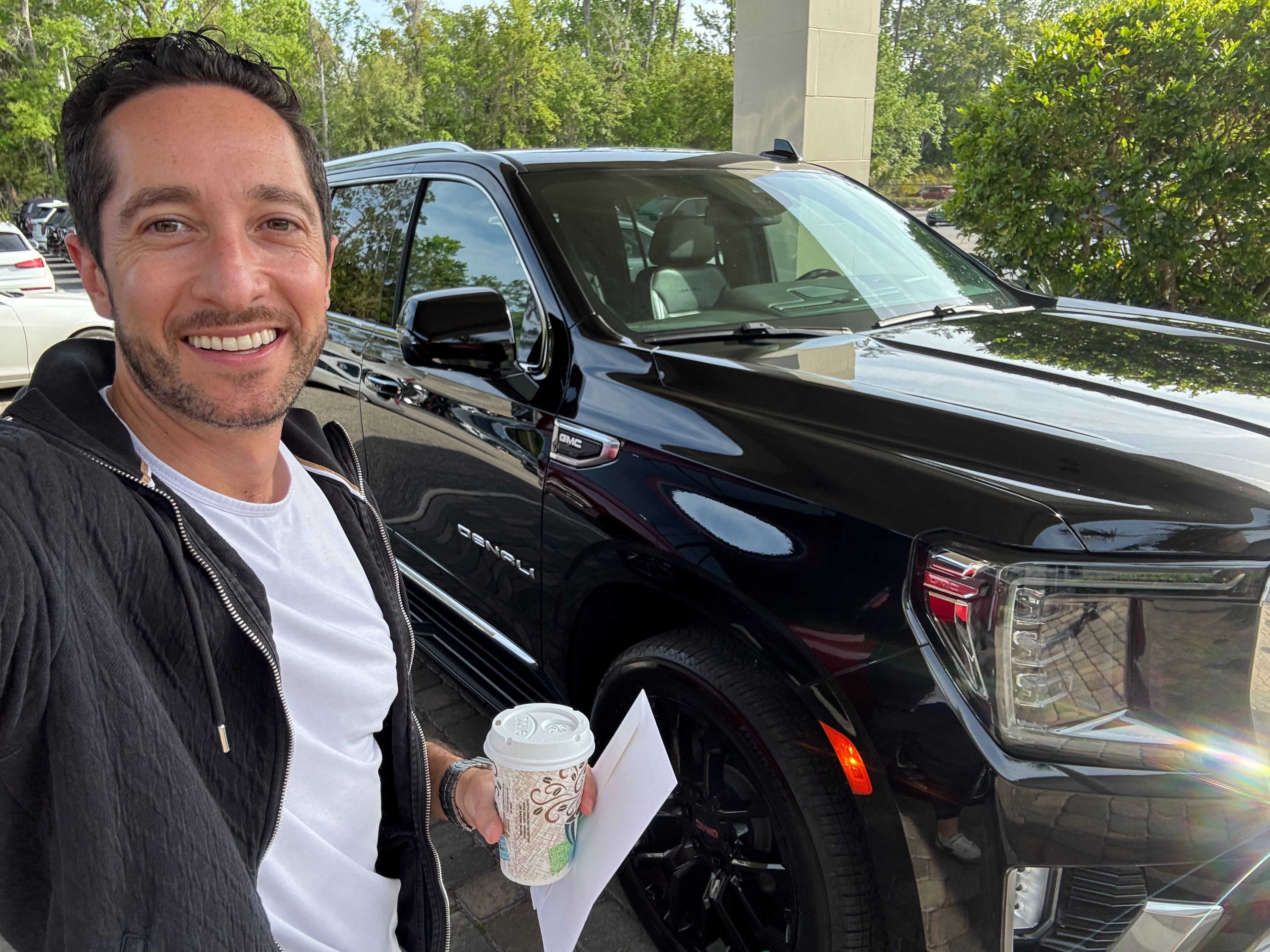Jeremy standing in front of the black GMC Yukon Denali on pickup day, coffee and paperwork in hand