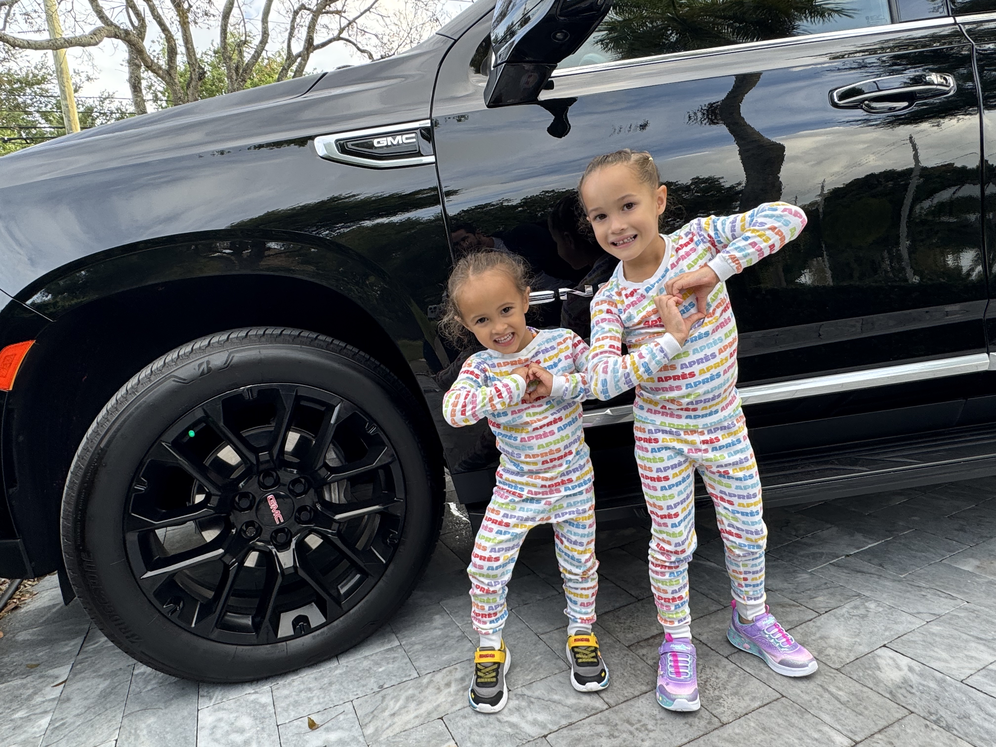 Two of the founder's kids in matching pajamas making heart shapes with their hands in front of the new black GMC Yukon